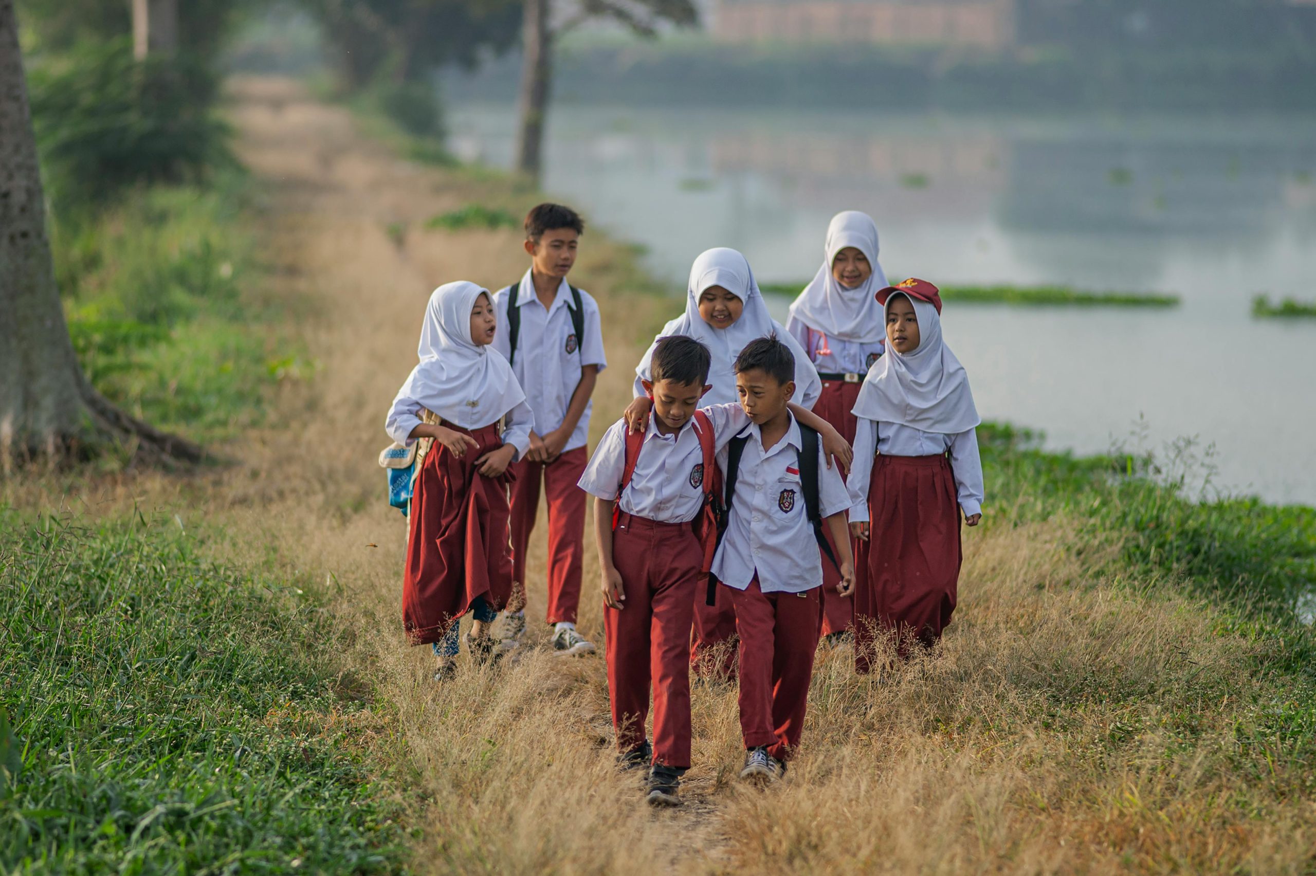 Home Group of children in school uniforms walking along a rural path in West Java, Indonesia.