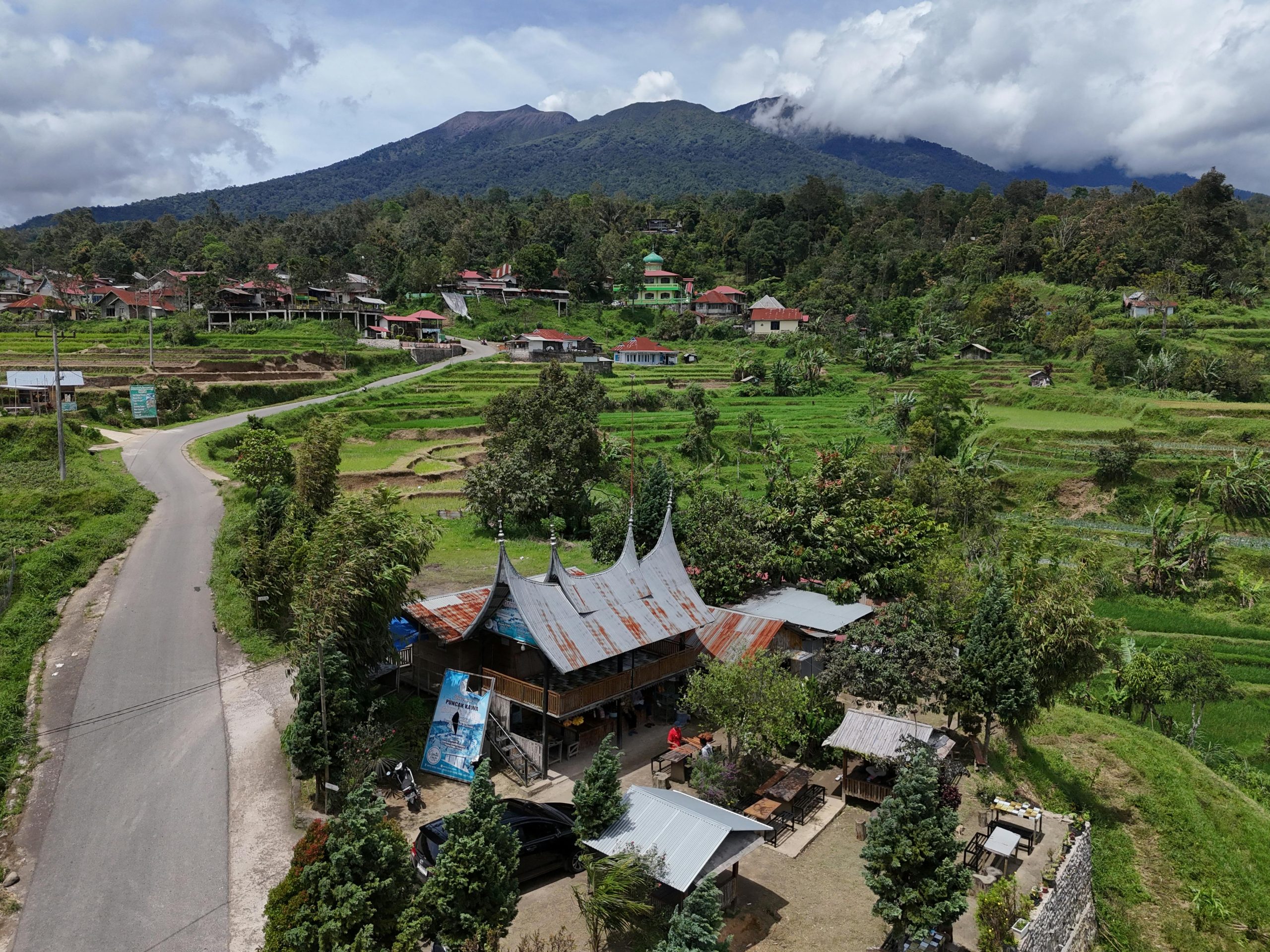 Home A beautiful aerial shot of a Minangkabau village with lush green rice fields and mountains in West Sumatra, Indonesia.